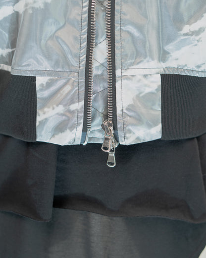 Close-up of a JKEEFER jacket detail showing a silver metallic zippered front, a light gray and white abstract patterned upper section, black ribbed trim, and a black lower section.