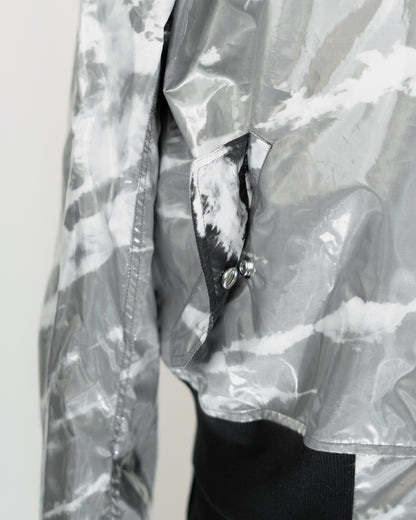 Close-up of a shiny silver-gray JKEEFER jacket with a white and gray tie-dye or marbled pattern, featuring a pocket with a black-and-white patterned flap and silver snap buttons.