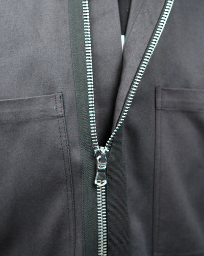 Close-up of a dark gray JKEEFER zippered jacket with a silver metal zipper and a black vertical trim panel running down the center.